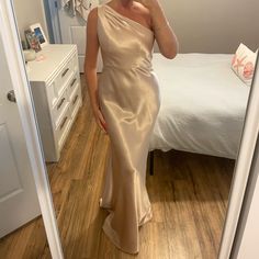 a woman taking a selfie in a mirror wearing a gold one - shoulder dress