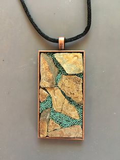 a square pendant with green and brown stones in it on a black leather cord necklace