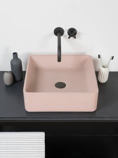 a pink sink sitting on top of a black counter next to a white vase and toothbrush holder