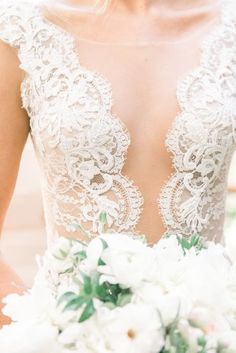 a woman in a wedding dress holding a bouquet with white flowers and greenery on it