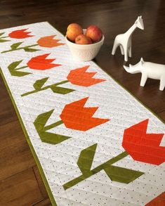 a table runner with an orange and green flower design on it next to a bowl of fruit