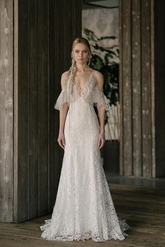 a woman in a white wedding dress standing on a wooden floor with her arms behind her back