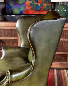 a green leather chair sitting in front of a painting on a wall next to a dresser