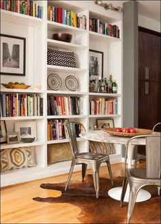 a dining room table and chairs in front of bookshelves with pictures on them