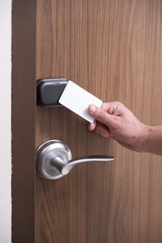 a hand holding a business card in front of a door handle on a wooden door