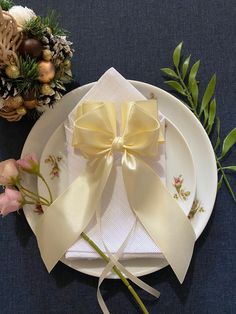 a white plate topped with a bow next to a bouquet of flowers and greenery