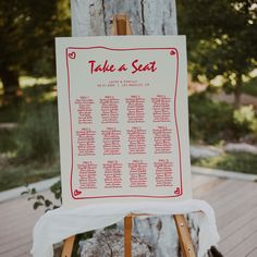 a wooden easel with a seating chart on it sitting in front of a tree