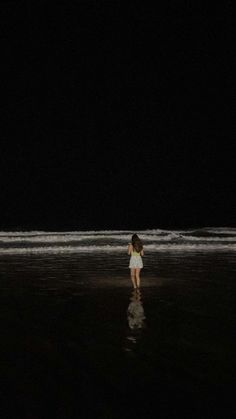 a woman standing on the beach at night with her back to the camera, looking out into the water