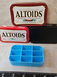 two tins of altoids sitting on top of a table next to a ruler