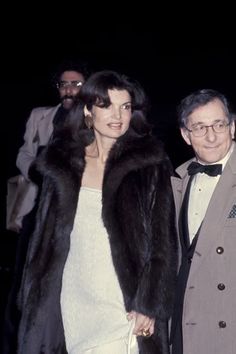 an old photo of two people dressed in formal wear and one is wearing a fur coat