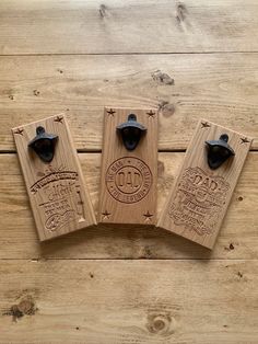 three wooden bottle openers with black handles on a wood background, one is engraved and the other has an emblem