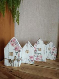 three wooden houses with flowers painted on them sitting next to a potted plant in front of a wall