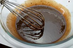 a whisk in a glass bowl filled with melted chocolate and other ingredients on a white table