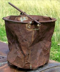 an old rusted out bucket sitting on top of a piece of wood with a stick sticking out of it