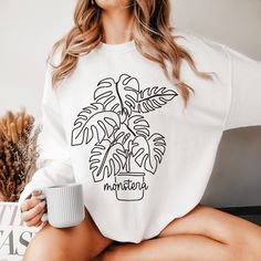 a woman holding a coffee cup and wearing a white shirt with a plant on it