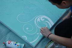 a woman is painting a large piece of art on the floor with blue and white paint