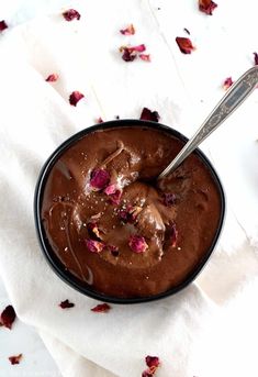 a bowl filled with chocolate pudding on top of a white cloth covered in rose petals