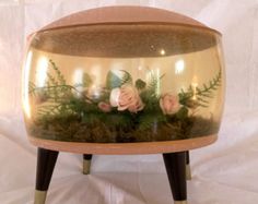 a vase filled with flowers and greenery on top of a wooden stand in front of a white backdrop