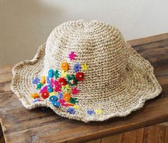 a straw hat with colorful flowers on it sitting on a wooden table next to a wall