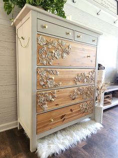 a white dresser with wooden drawers and flowers on it