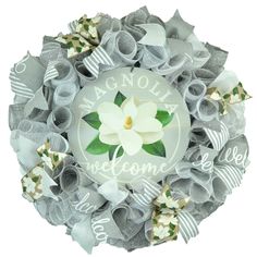 a white flower with green leaves is on a gray mesh wreath that says magnolia welcome