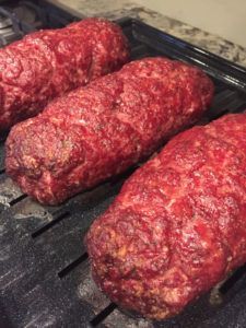 three raw meat patties cooking on an open grill