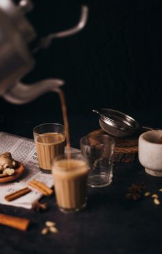 a table topped with glasses and cinnamons next to a teapot filled with liquid