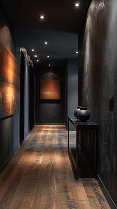 a long hallway with wooden floors and black walls, along with a vase on the end table