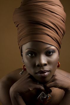 a woman in a brown turban poses for a photo with her hands on her chin