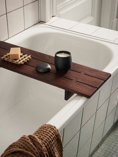 a bath tub with a wooden shelf next to it and a candle on the edge