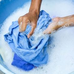 a person washing their hands in a blue bucket filled with foam and water, while holding a rag