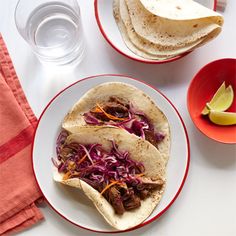 two tacos with meat, cabbage and orange slaw are on a white table