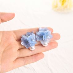 a hand holding two tiny blue flowers and pearls