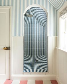 a bathroom with blue and white stripes on the walls, shower stall and rug in the floor