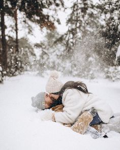 a woman laying in the snow with her head on another woman's shoulder and kissing her forehead