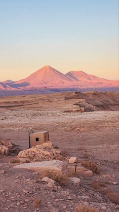 a desert with mountains in the background and rocks on the ground, there is a small structure that has been built into it