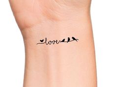 a small wrist tattoo with birds sitting on top of the word love written in cursive writing