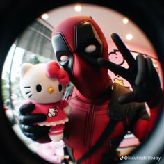 a hello kitty doll is posed in front of a deadpool character with her hand up to the camera