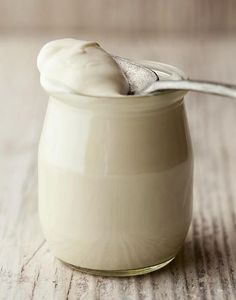 a glass jar filled with cream on top of a wooden table next to a spoon