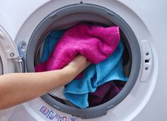 a person holding a pink and blue towel in front of a washing machine with it's door open