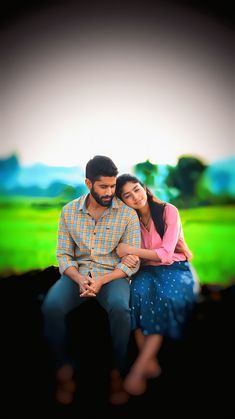 a man and woman sitting next to each other in front of a green grass field