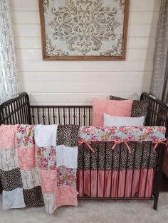 a baby crib with pink, brown and white bedding in front of a painting