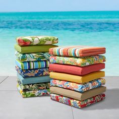 a stack of colorful pillows sitting on top of a table next to the ocean and beach