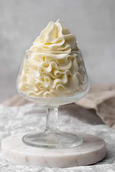 a glass bowl filled with whipped cream on top of a white table cloth next to a napkin