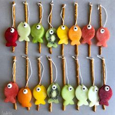 several different colored fish ornaments are hanging on twig sticks with toothpicks attached to them