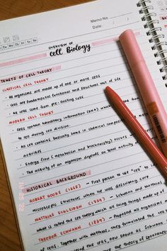 two pink pens sitting on top of an open notebook