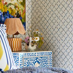 a blue and white dresser with flowers on it in front of a floral wallpaper