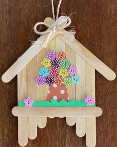 a wooden house shaped like a tree with flowers on the front and side, hanging from a string