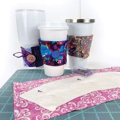 three coffee cups sitting on top of a table next to a piece of cloth and scissors