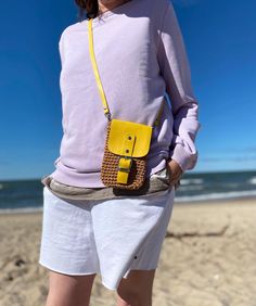 a woman is standing on the beach with her hand in her pocket and she has a yellow purse over her shoulder